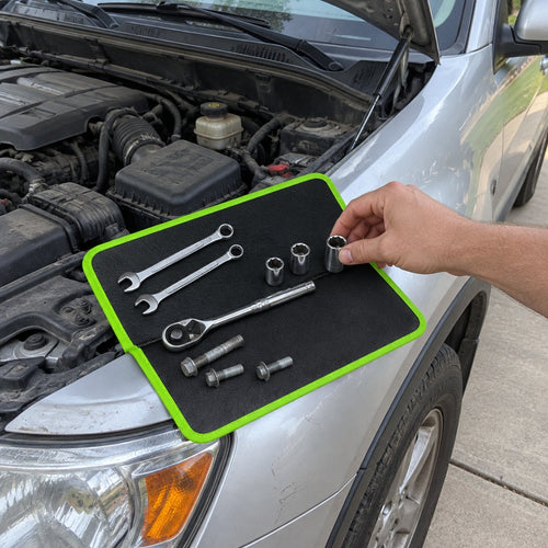 Folding magnetic tool mat open on a car fender holding wrenches, a ratchet, sockets and bolts